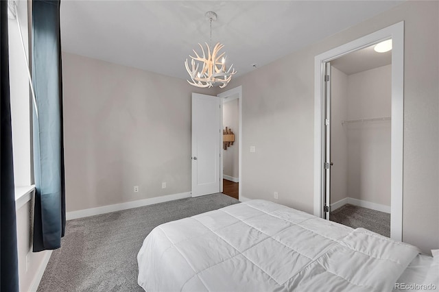 bedroom with dark colored carpet, a spacious closet, and an inviting chandelier