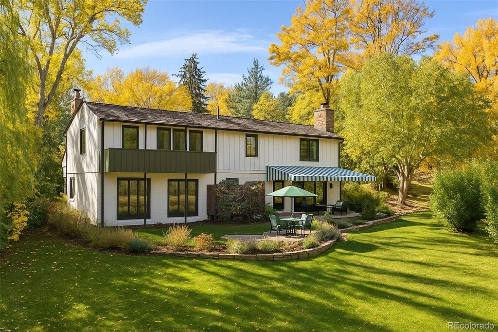 back of house featuring a patio area, a yard, board and batten siding, and a chimney