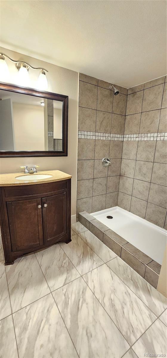 12388 Jasmine St, Brighton, CO 80602 - bathroom featuring marble finish floors, a tile shower, and vanity
