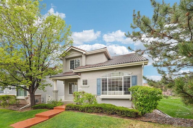 view of front of property featuring stucco siding, a front lawn, and a tile roof