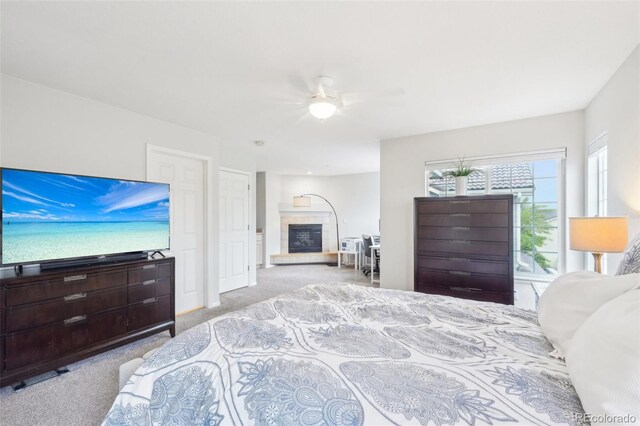 carpeted bedroom featuring a tiled fireplace and a ceiling fan