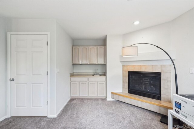 unfurnished living room with carpet floors, a tiled fireplace, baseboards, a sink, and recessed lighting