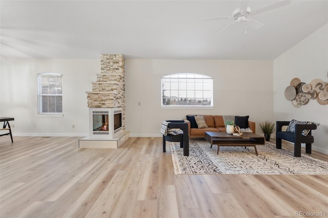 living room with a stone fireplace, light hardwood / wood-style floors, and ceiling fan