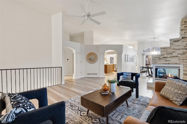 living room featuring ceiling fan, a stone fireplace, lofted ceiling, and light wood-type flooring