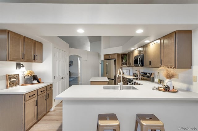 kitchen with sink, a breakfast bar, appliances with stainless steel finishes, kitchen peninsula, and light wood-type flooring