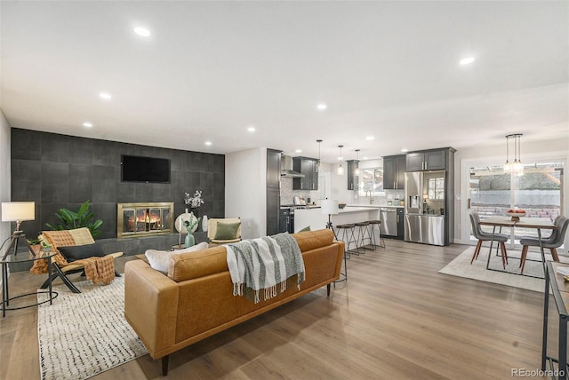 living area with recessed lighting, an accent wall, wood finished floors, a tile fireplace, and plenty of natural light