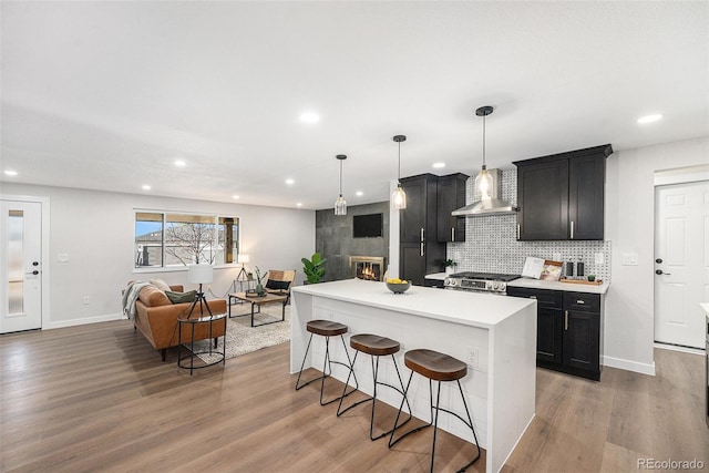 kitchen featuring wood finished floors, a kitchen breakfast bar, open floor plan, wall chimney range hood, and decorative backsplash