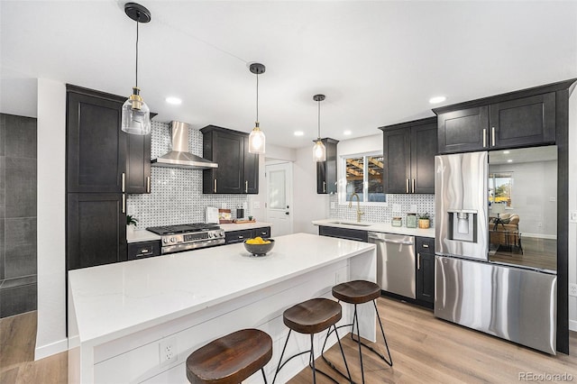 kitchen with light wood-style floors, a center island, stainless steel appliances, wall chimney range hood, and a sink