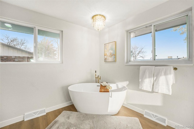 full bath featuring a soaking tub, wood finished floors, visible vents, and baseboards