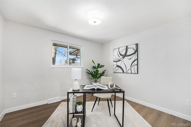 office with visible vents, a textured ceiling, baseboards, and wood finished floors