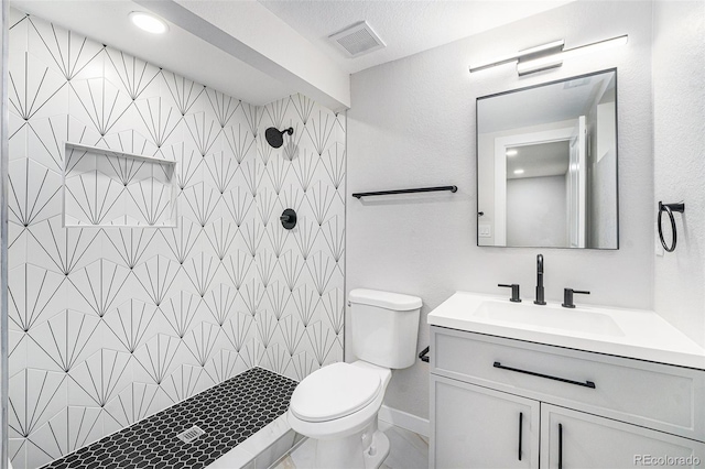 full bath with toilet, vanity, visible vents, and a tile shower