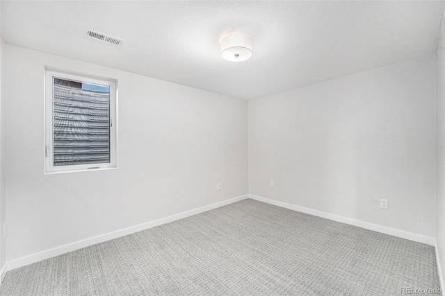 empty room with carpet floors, visible vents, a textured ceiling, and baseboards