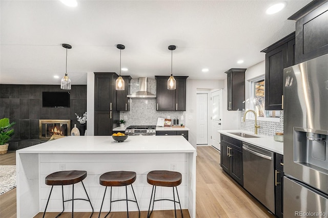 kitchen featuring a sink, light wood-style floors, a kitchen breakfast bar, appliances with stainless steel finishes, and wall chimney exhaust hood