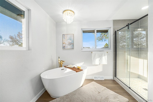 bathroom with baseboards, visible vents, wood finished floors, a freestanding bath, and a shower stall