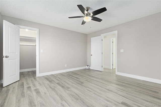 unfurnished bedroom featuring ceiling fan, light hardwood / wood-style floors, a textured ceiling, a walk in closet, and a closet