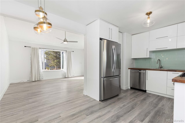 kitchen featuring butcher block counters, light hardwood / wood-style flooring, decorative backsplash, appliances with stainless steel finishes, and white cabinetry