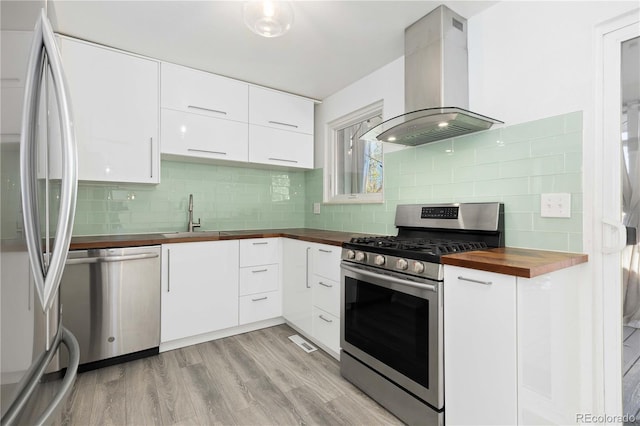 kitchen featuring exhaust hood, sink, appliances with stainless steel finishes, butcher block countertops, and light hardwood / wood-style floors