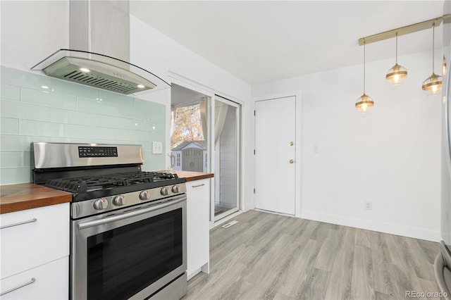 kitchen featuring stainless steel gas range oven, white cabinets, butcher block countertops, hanging light fixtures, and range hood