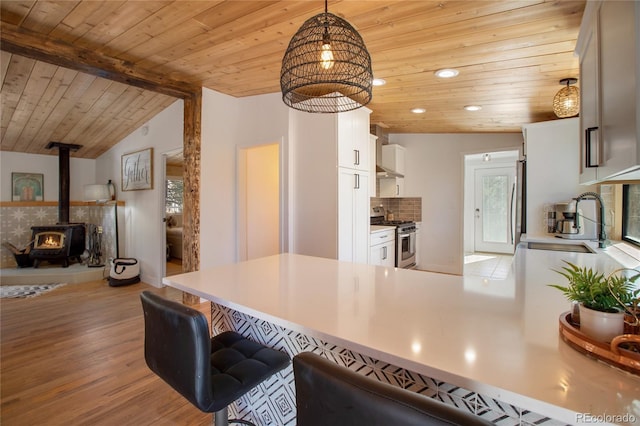 kitchen featuring vaulted ceiling with beams, kitchen peninsula, stainless steel appliances, a wood stove, and white cabinets