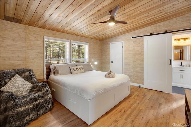 bedroom with ceiling fan, a barn door, light wood-type flooring, vaulted ceiling, and ensuite bathroom