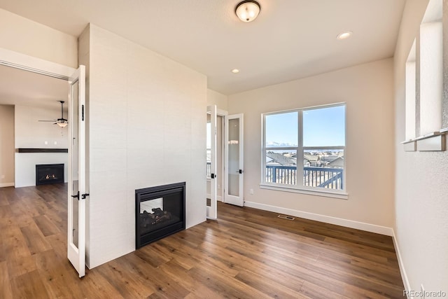 unfurnished living room with baseboards, visible vents, a multi sided fireplace, and wood finished floors