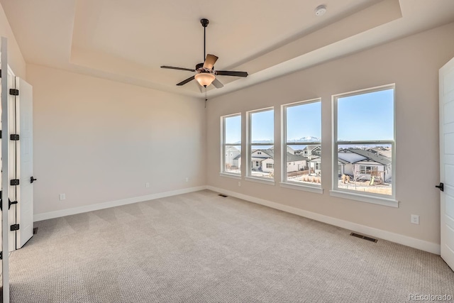 spare room featuring a raised ceiling, visible vents, light carpet, and baseboards