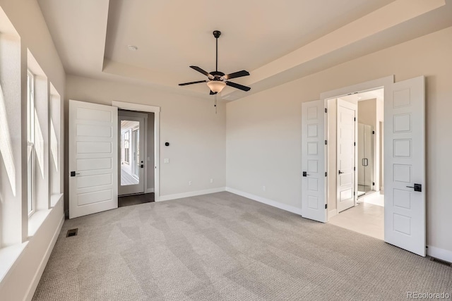 carpeted spare room featuring ceiling fan, a raised ceiling, visible vents, and baseboards