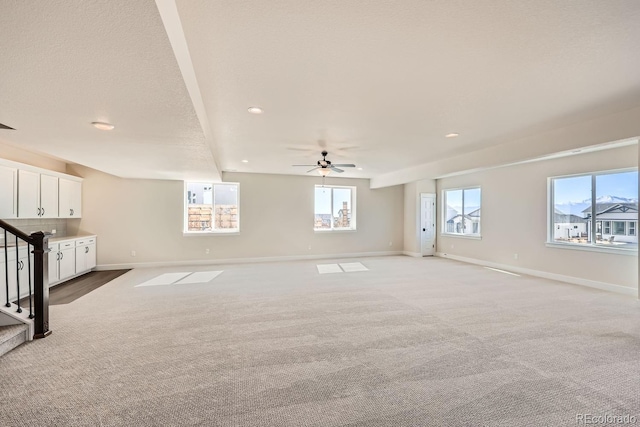 unfurnished living room featuring a textured ceiling, stairway, light colored carpet, and baseboards