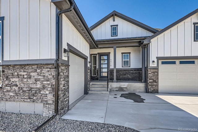 view of exterior entry featuring an attached garage, stone siding, driveway, and board and batten siding