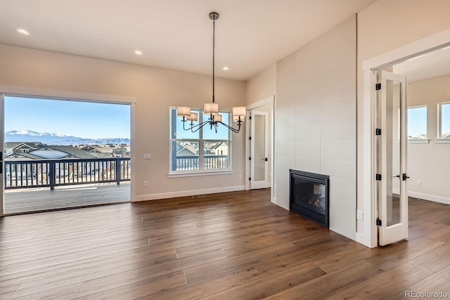 unfurnished dining area featuring baseboards, a tiled fireplace, wood finished floors, an inviting chandelier, and recessed lighting