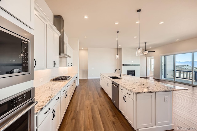 kitchen with white cabinets, appliances with stainless steel finishes, wood finished floors, wall chimney range hood, and a sink