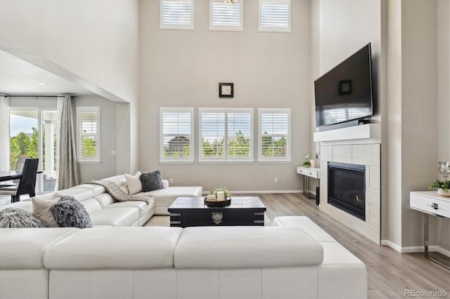 living room featuring a towering ceiling, a tiled fireplace, and light hardwood / wood-style flooring