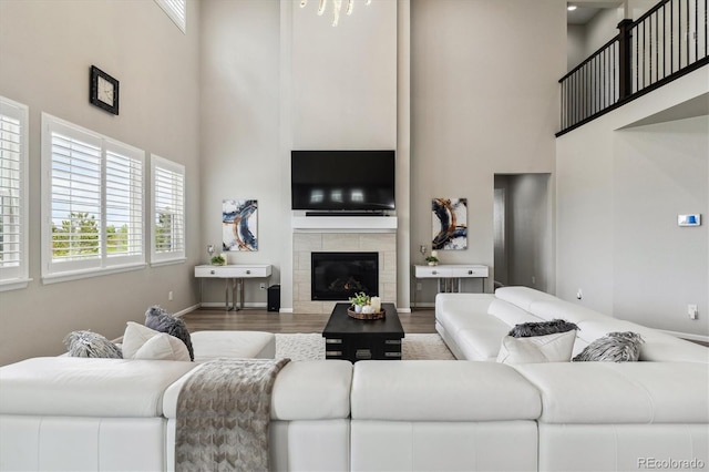 living room with a tiled fireplace, a towering ceiling, and hardwood / wood-style flooring