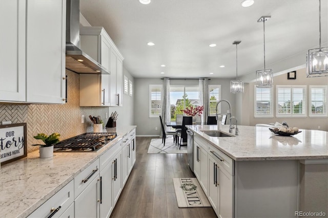 kitchen with decorative light fixtures, dark wood-type flooring, wall chimney exhaust hood, a kitchen island with sink, and sink