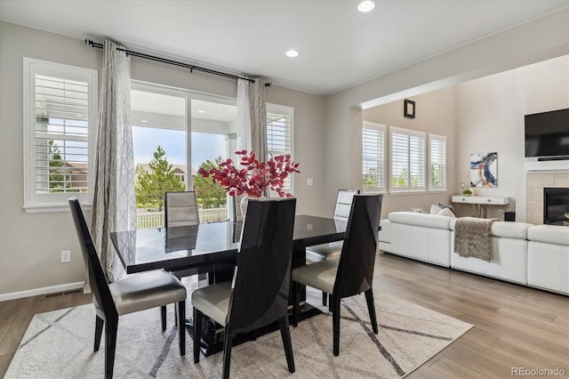 dining area featuring a tiled fireplace, plenty of natural light, and light wood-type flooring