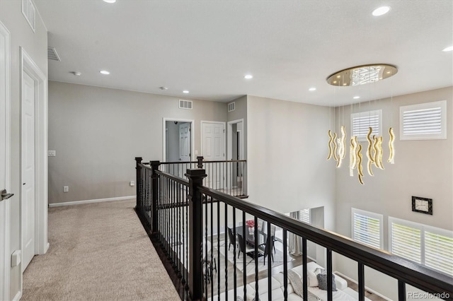 corridor featuring an inviting chandelier and light carpet