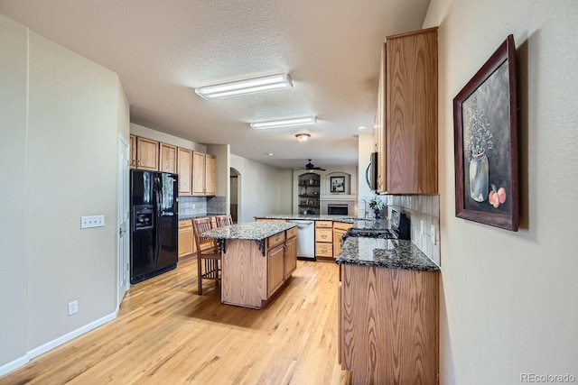 kitchen with a kitchen breakfast bar, backsplash, a kitchen island, black appliances, and light wood-type flooring