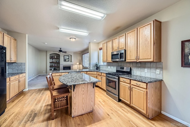 kitchen featuring kitchen peninsula, appliances with stainless steel finishes, a kitchen bar, light wood-type flooring, and dark stone countertops