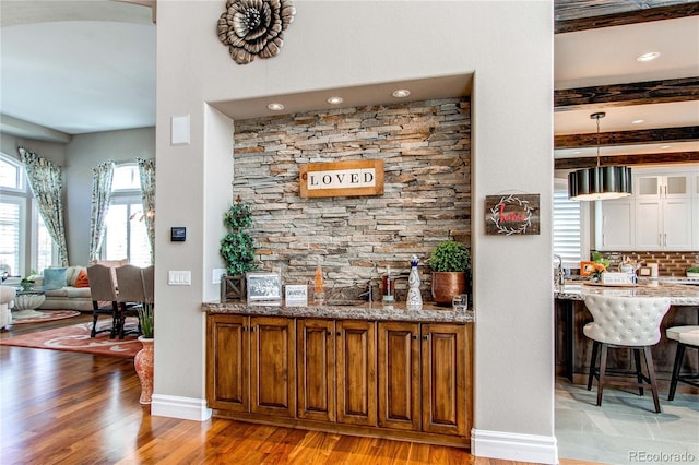 bar with beam ceiling, light stone counters, pendant lighting, light hardwood / wood-style floors, and decorative backsplash