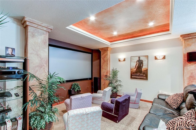 home theater room with a textured ceiling, a tray ceiling, and decorative columns