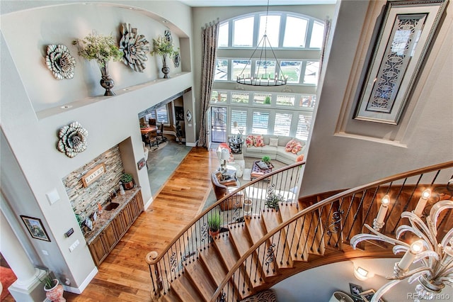 stairway featuring a towering ceiling, wood-type flooring, and an inviting chandelier