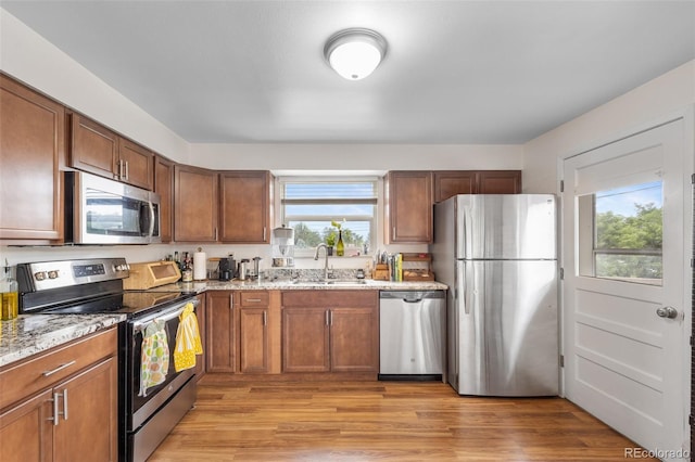 8485 W 44th Ave, Wheat Ridge, CO 80033 - kitchen featuring appliances with stainless steel finishes, light stone counters, light wood finished floors, and brown cabinetry