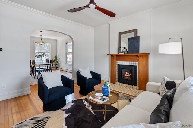 living area with a baseboard radiator, a fireplace, arched walkways, ornamental molding, and hardwood / wood-style flooring