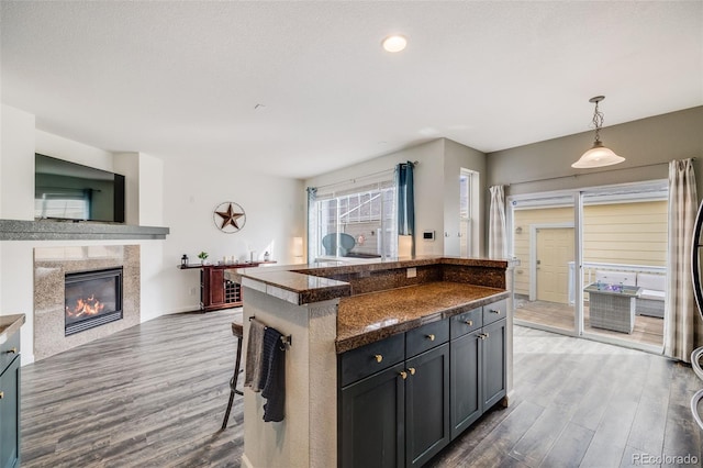 22765 E Ottawa Pl, Aurora, CO 80016 - kitchen with wood finished floors, dark countertops, a breakfast bar, and a tiled fireplace