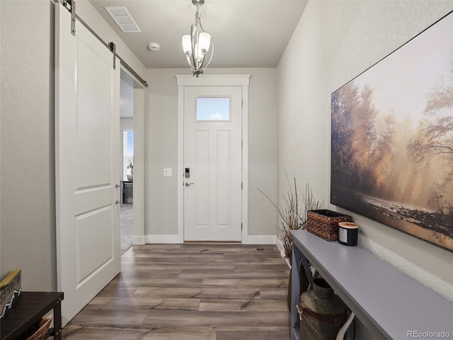 foyer entrance with baseboards, a barn door, visible vents, and wood finished floors