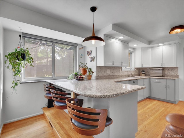 4720 W Stanford Ave, Denver, CO 80236 - kitchen with a peninsula, light wood-type flooring, decorative backsplash, a breakfast bar, and light stone counters