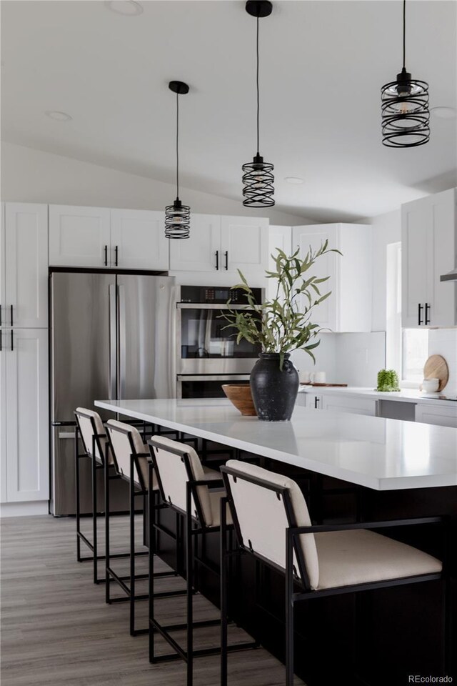 8249 Zephyr St, Arvada, CO 80005 - kitchen featuring appliances with stainless steel finishes, light wood-style floors, white cabinetry, light countertops, and vaulted ceiling