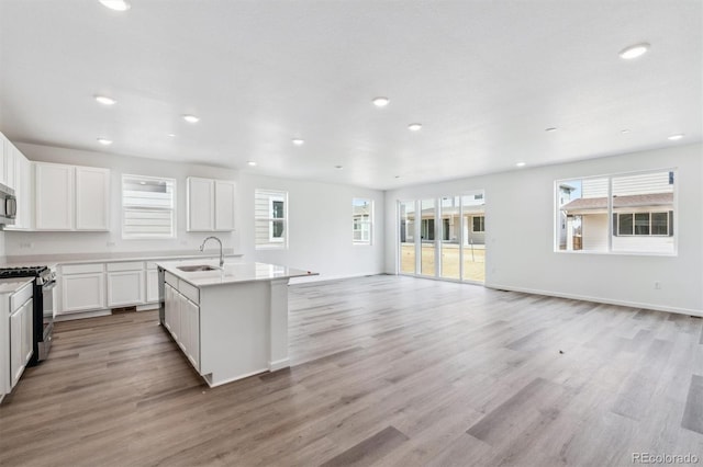 kitchen featuring a sink, range with gas cooktop, open floor plan, light wood-type flooring, and a kitchen island with sink