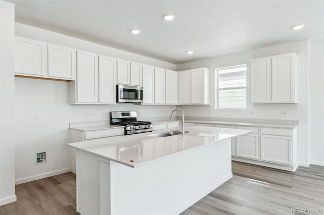 kitchen with a center island with sink, a sink, white cabinetry, stainless steel appliances, and light wood-style floors