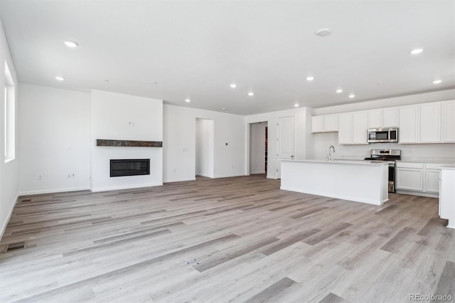 unfurnished living room with a glass covered fireplace, recessed lighting, light wood-style flooring, and visible vents